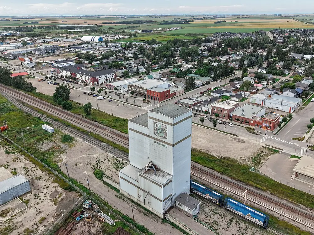 Aerial view of Crossfield with a white grain elevator beside the railway tracks and the town behind it