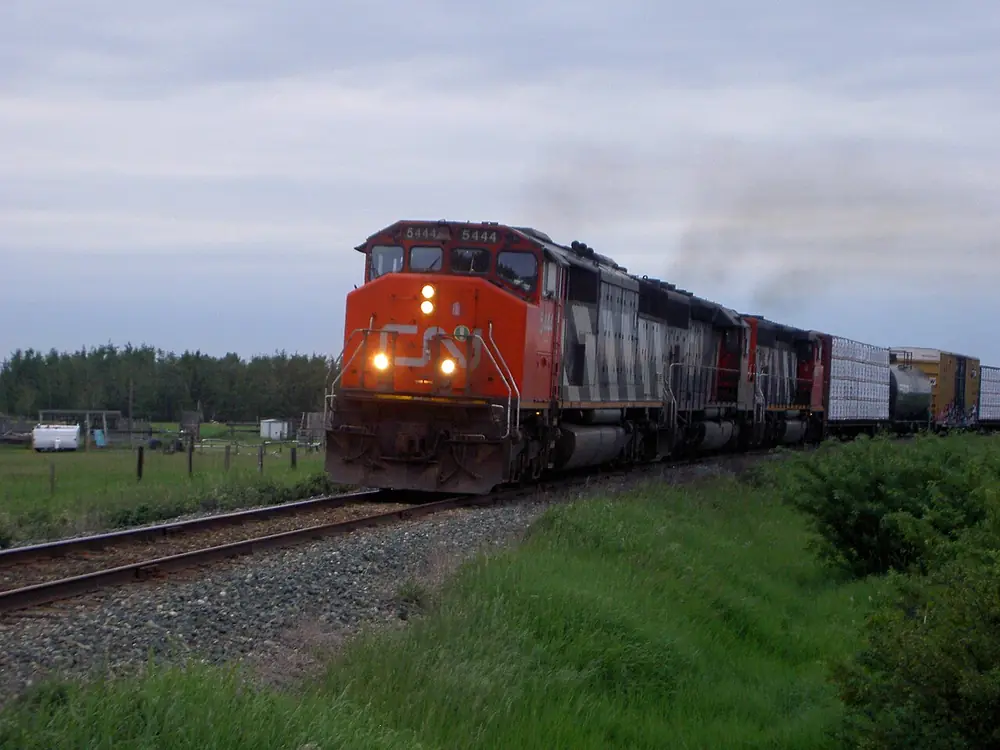 A red CN locomotive pulling a freight train across green prairie near Irricana